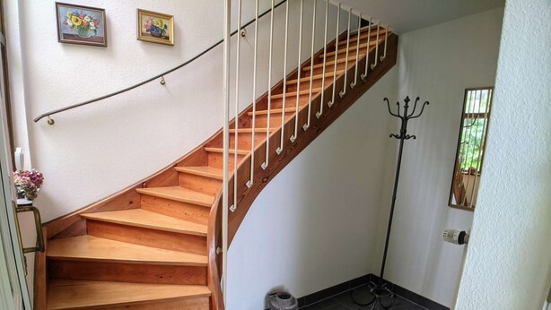 A wooden staircase with a white railing, leading to an upper floor. There are two framed pictures on the wall above the stairs.