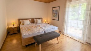 A bedroom with a wooden ceiling, a bed with floral bedding, a bench, and a window with curtains.
