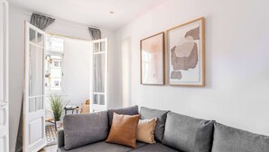 A modern living room with a grey sectional sofa, two framed abstract paintings, and a view into a connected space. - Sunny 4BD apartment in Sagrada Familia (Barcelona)