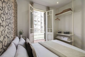 A bedroom with a bed, a wardrobe, a hanging rack, and a view of an apartment building through an open door. - Sunny 4BD apartment in Sagrada Familia (Barcelona)