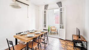A dining area with a wooden table set for four, chairs, an air conditioning unit, and a television on a side table. - Sunny 4BD apartment in Sagrada Familia (Barcelona)