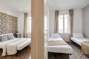 Een hotelkamer met drie bedden, een behang met patroon en uitzicht door een raam.