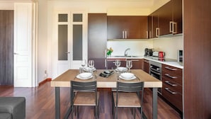 Une cuisine moderne avec des meubles en bois, une table à manger pour deux personnes et un petit îlot central doté d’un évier.