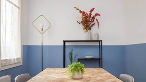 Une salle de conférence avec une table en bois, des chaises, une plante en pot, un lampadaire et une étagère ornée d’objets décoratifs.