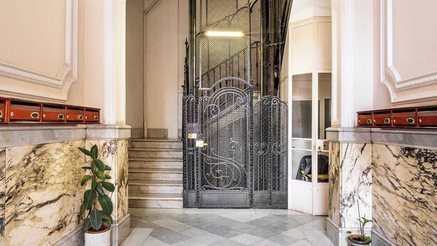Un vaste hall aux murs de marbre, orné d’un lustre et doté d’un escalier menant à l’étage supérieur.