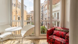 A room with large windows, a white table with two chairs, and a red floral sofa. - Paseo de Gracia | Classy 3bed 3bath apartment (Barcelona)