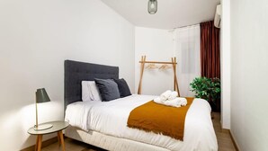 A neatly arranged bedroom with a bed, bedside table, lamp, and a drying rack.