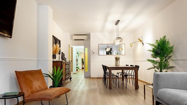 A modern living room with a leather chair, a grey sofa, a dining table with chairs, a black rug, and a potted plant.