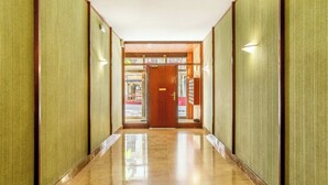 Un couloir se termine par une porte en bois, de part et d’autre de laquelle s’étendent des murs verts à texture et un sol carrelé brillant.