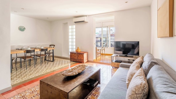 Een moderne woonkamer met een bank, salontafel, televisie en een eethoek met stoelen en een tafel.