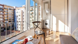 Een balkon met uitzicht op omliggende gebouwen, een stoel, een tafel met servies en een wasmachine.