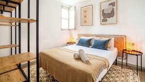 Een hotelkamer met een bed, een houten plank, een raam en een kunstwerk in een lijst aan de muur.