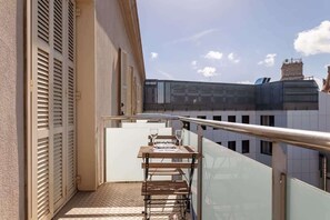 A balcony with a table and chairs, a metal railing, and a building with windows in the background.
