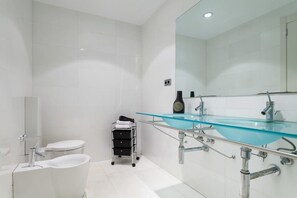 A modern bathroom with a glass sink, a toilet, and a bidet.