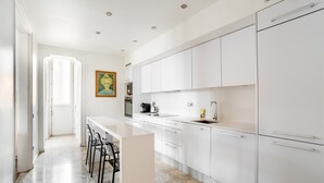 Une cuisine moderne avec des meubles blancs, un plan de travail en marbre et un coin bar avec des tabourets.