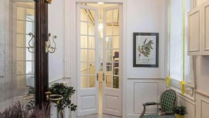 A room with a wooden floor, a green upholstered chair, a round table, a large mirror, and a chandelier. - Amazing 5Bd for 13 with terrace in Plaza Cataluña (Barcelona)