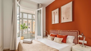 A hotel room with a large bed, a bedside table with a lamp, a window with curtains, and a view of buildings outside. - Private Terrace 4-bedroom apartment in Eixample (Barcelona)