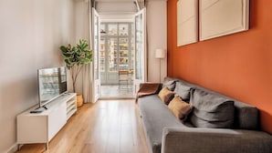 A modern living room with a grey sofa, a flat-screen TV on a white stand, and a ceiling fan. - Private Terrace 4-bedroom apartment in Eixample (Barcelona)