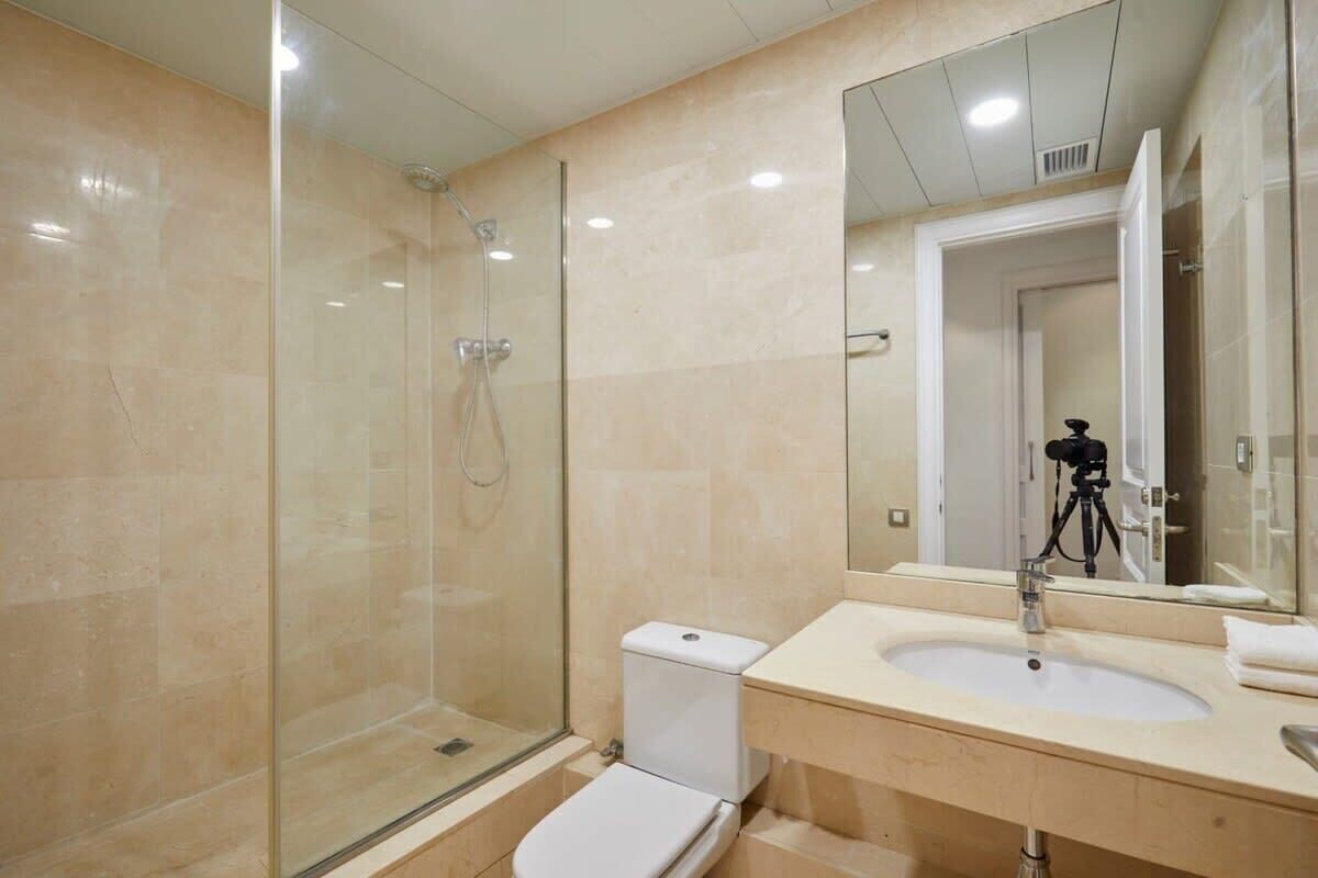 Un baño moderno con cabina de ducha de vidrio, inodoro blanco y lavamanos con espejo.