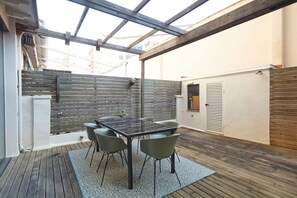 Une terrasse couverte avec une table et des chaises, un plancher en bois et une structure de toit en métal.