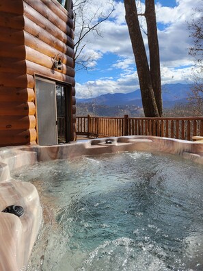 Une cabane en bois avec un jacuzzi et une vue sur les montagnes.