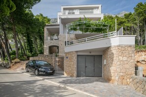 A modern two-story house with a stone facade, a balcony with greenery, and a car parked in front. - Villa Brela Apartment 1 (Brela)