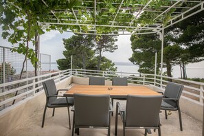 Ein Außenbereich zum Sitzen mit Tisch und Stühlen, umgeben von einem weißen Geländer, mit Blick auf ein Gewässer.