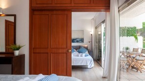 A hotel room with a wooden door, a bed with white and blue bedding, a small table with a plant, and a view of a balcony with outdoor furniture. - Golden Mile Apartment 150 m. to the beach (Marbella)