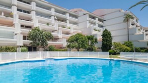 A swimming pool with a white fence, surrounded by multi-story buildings with balconies and greenery. - Golden Mile Apartment 150 m. to the beach (Marbella)
