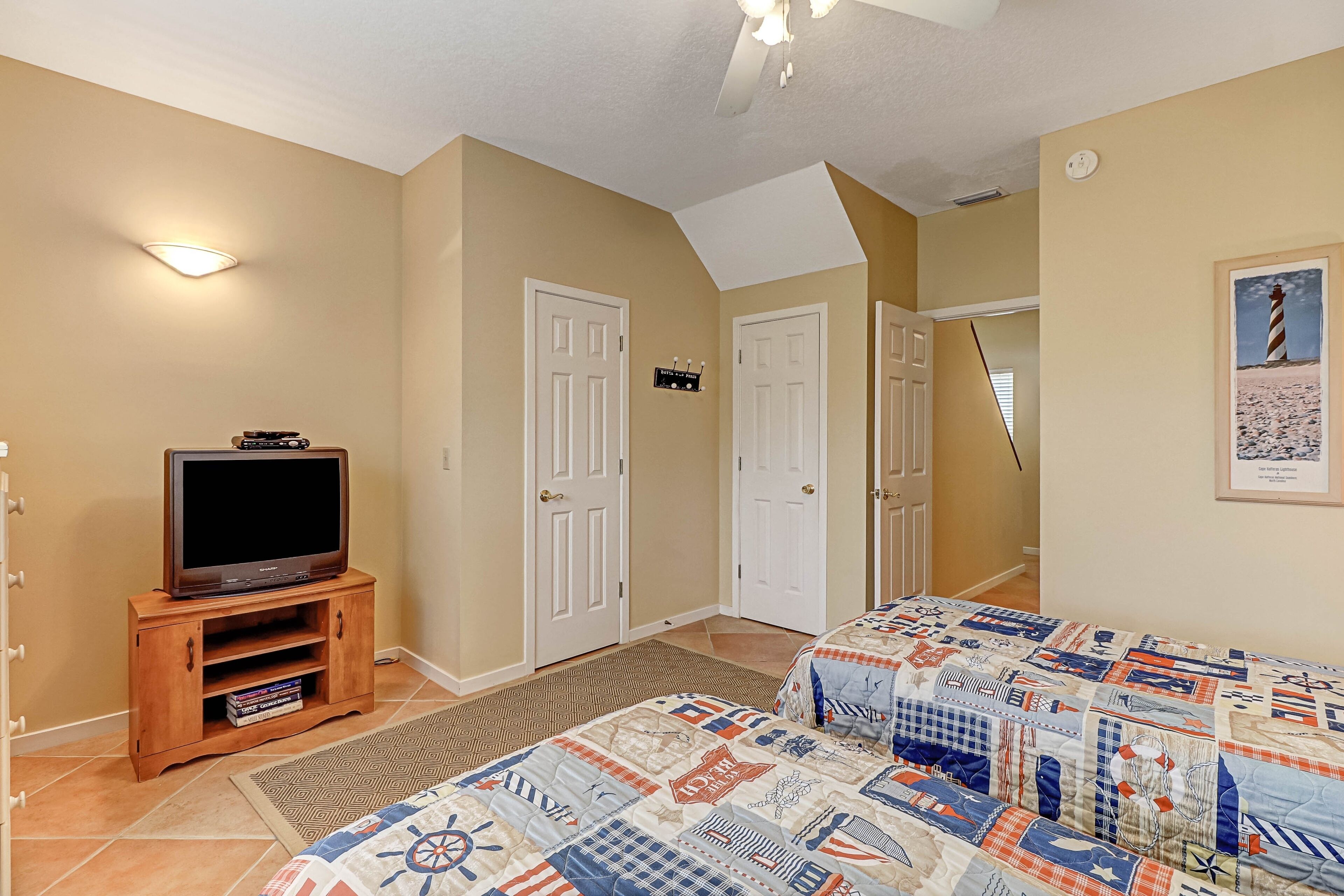 A bedroom with a bed, a television on a wooden stand, and a door leading to another room.