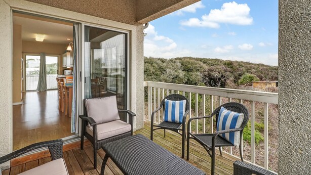 A balcony with wicker furniture, a view of the landscape, and a sliding glass door leading to an indoor area.