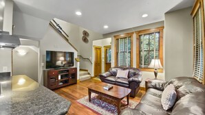 A living room with a TV, leather sofas, a coffee table, and a dining area with a granite countertop. - Ridge Street Chalet B 2 Bedroom Townhouse by RedAwning (Breckenridge)