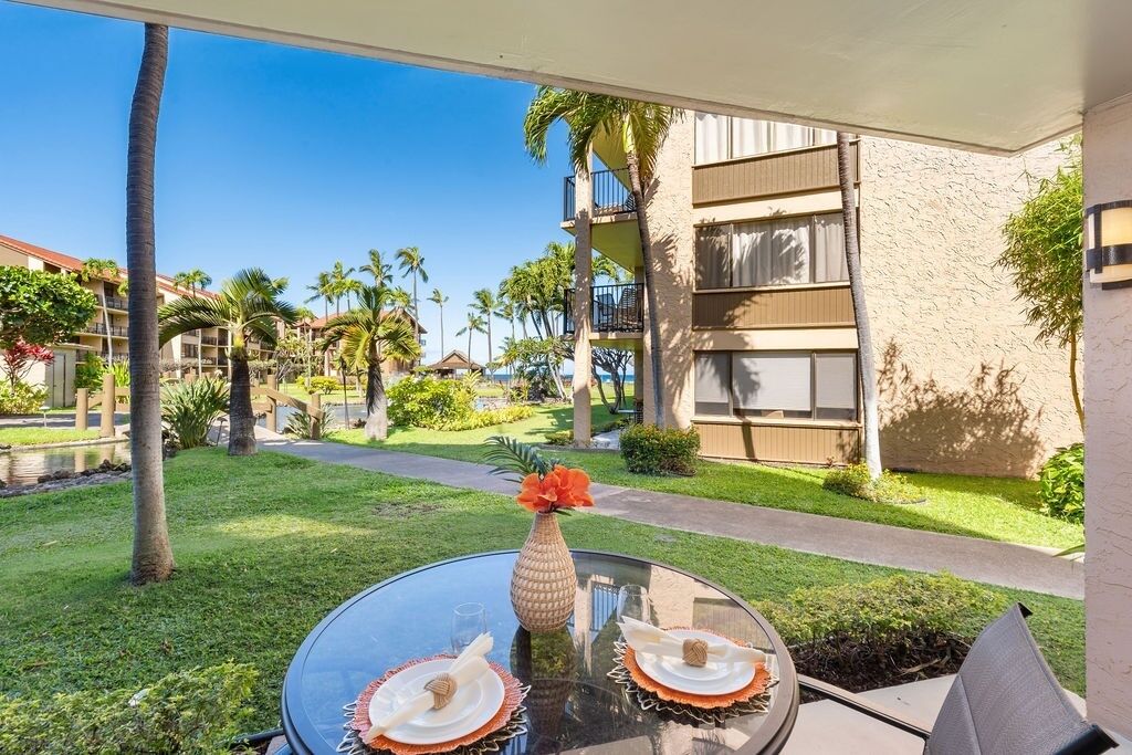 A glass table with a vase and plates, a pathway, and a building with balconies.