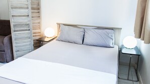 A neatly made bed with a wooden headboard, two bedside tables with round lamps, and a curtain on the window. - Cozy and Comfy Central Athens Apt. (Athens)