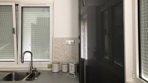 Une cuisine moderne avec un réfrigérateur noir, un évier en acier inoxydable et des stores à vitrage dépoli.