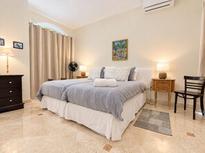 A bedroom with a bed, bedside tables, a chair, a dresser, a fan, and a painting on the wall.
