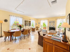 A spacious living area with a dining table, chairs, a sofa, and a television. There are books and decorative items on the table and shelves.