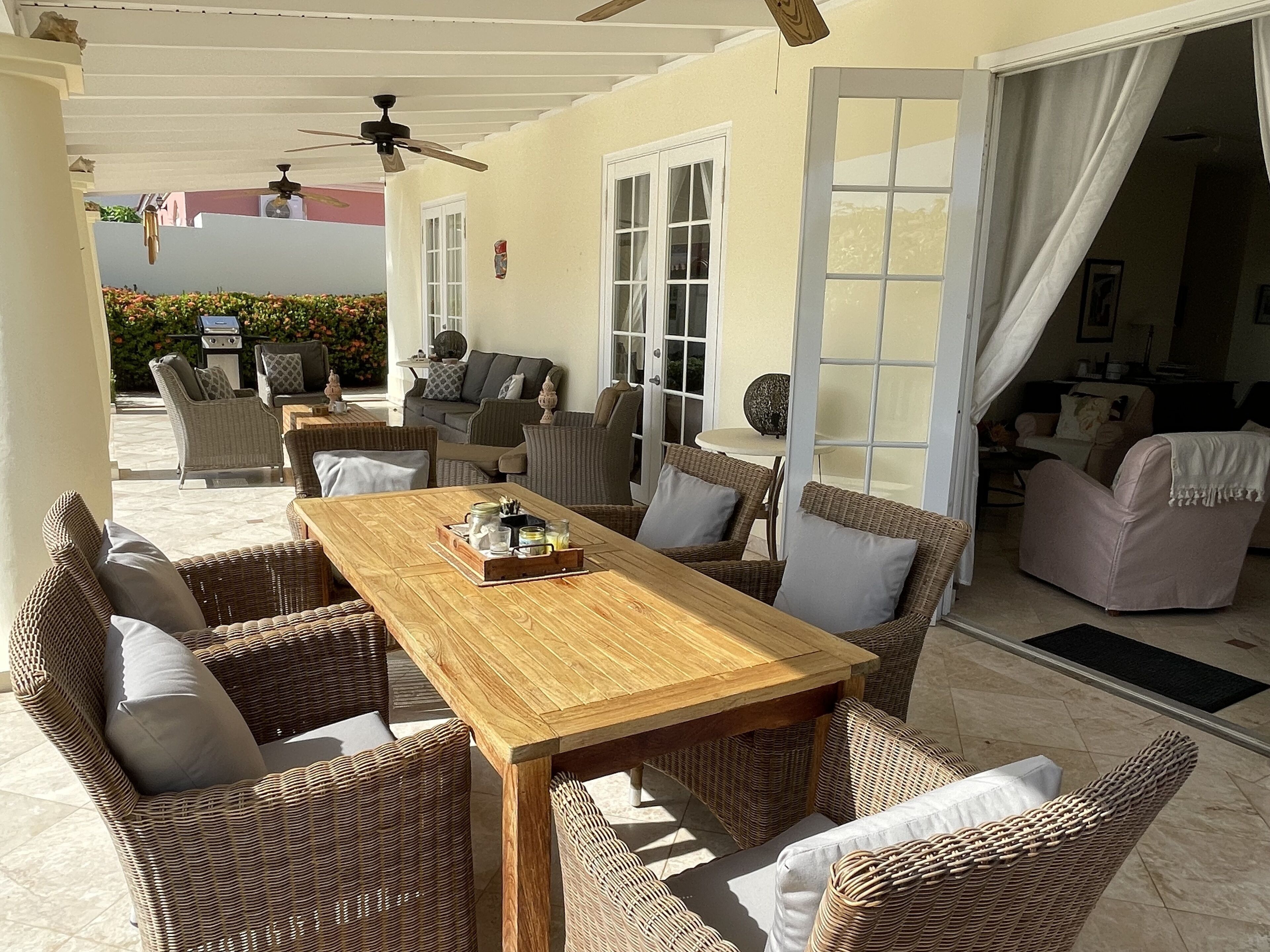 Patio esterno con mobili in vimini, tavolo in legno e ventilatori a soffitto.