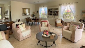 A spacious living room with a dining area, a bookshelf, and a large window with curtains. - Slice of Heaven at Tierra Del Sol - Sleeps 6 - Private Pool - On Golf Course (Noord)