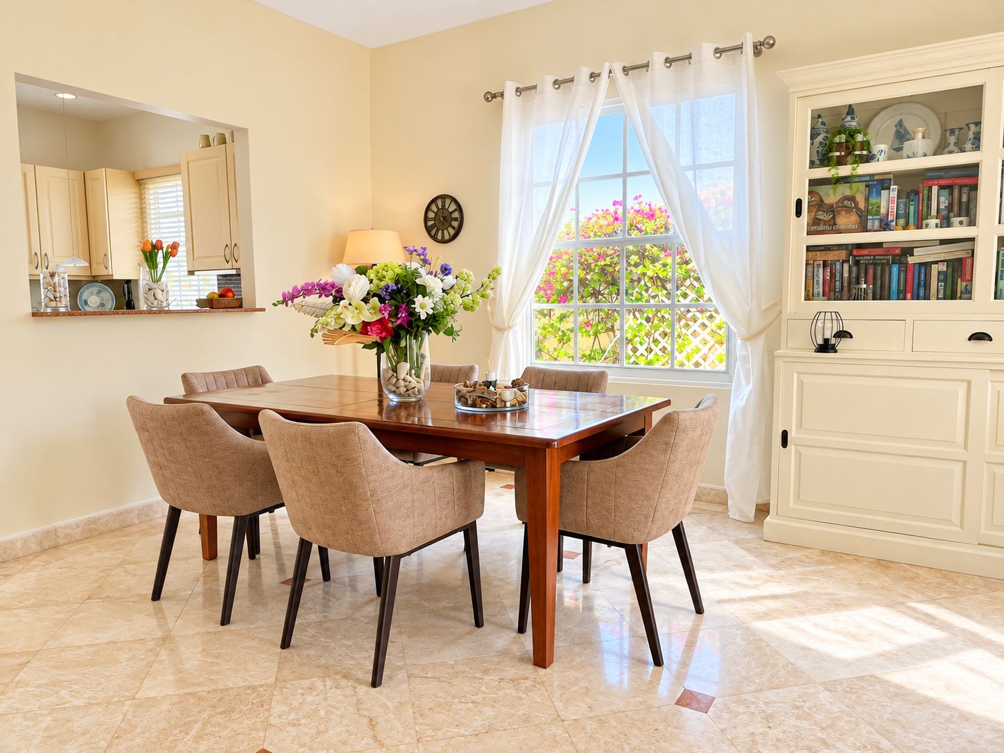 Un coin repas avec une table en bois et quatre chaises, un vase de fleurs, une horloge au mur et une fenêtre avec des rideaux.