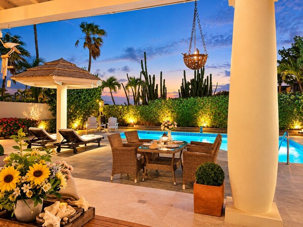 An outdoor pool area with lounge chairs, a table, and a hanging light fixture.
