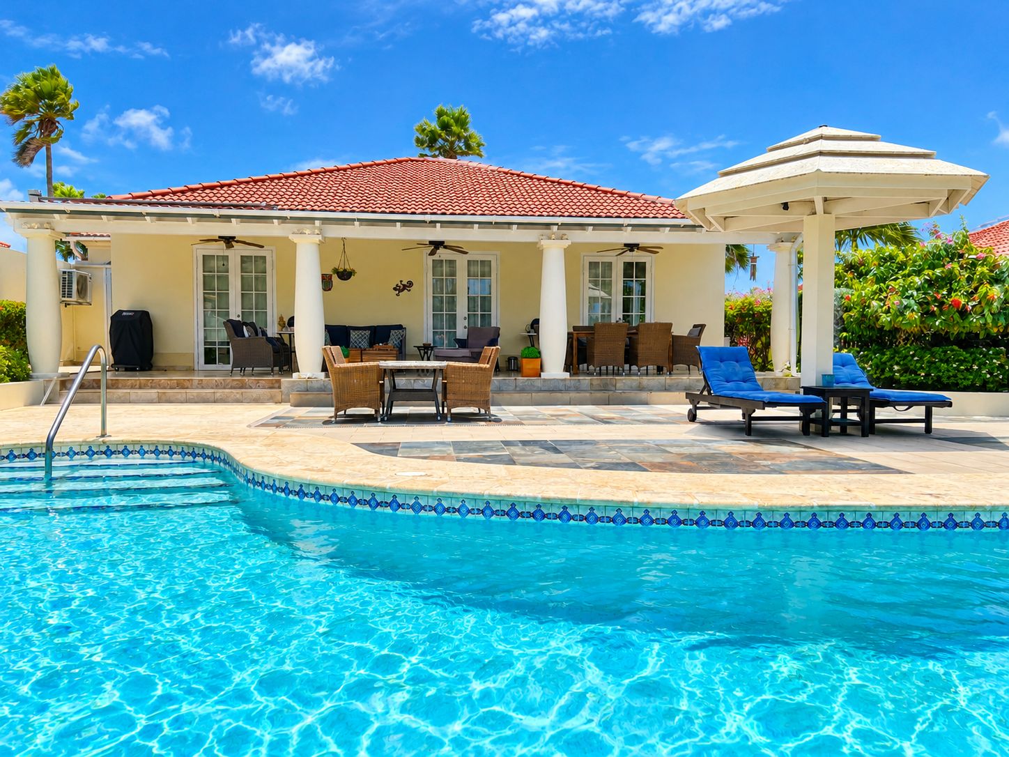 A swimming pool with lounge chairs and a covered seating area.