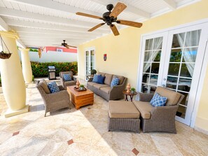 A covered outdoor seating area with wicker furniture, a ceiling fan, and a view of the outside.