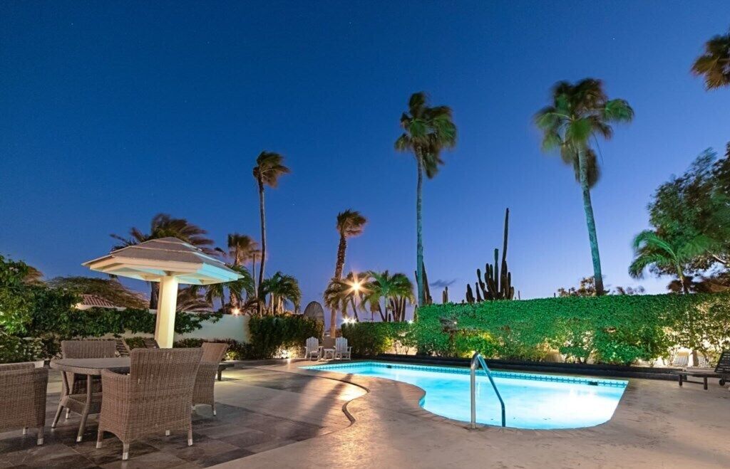 A pool area with lounge chairs and a table, surrounded by palm trees and greenery.