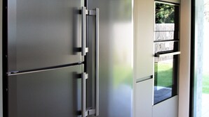 Une cuisine moderne équipée d’un réfrigérateur en acier inoxydable, d’un four encastré et d’une fenêtre donnant sur l’extérieur.