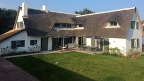 Une maison avec un toit à forte pente, un patio couvert aménagé avec du mobilier d’extérieur et une pelouse bien entretenue.