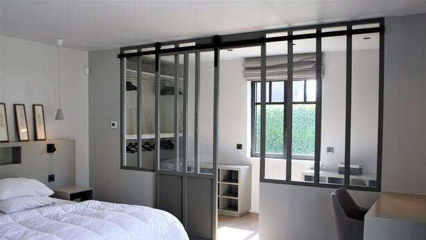 Une chambre moderne avec un lit, un bureau et une chaise. Une grande fenêtre laisse entrer la lumière naturelle et offre une vue sur la verdure environnante.
