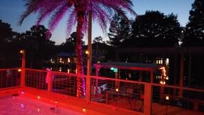 A pool area with a palm tree, a fenced deck, and a building in the background. - Waterfront 4 bedroom. Discount available for extended or monthly rentals! (Slidell)