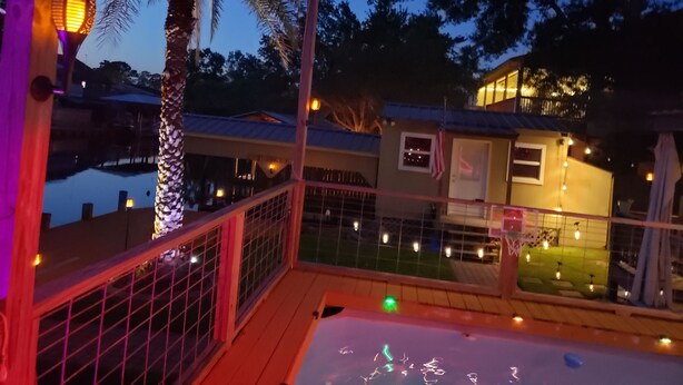 A deck with a railing, a palm tree, and a building with string lights. - Waterfront 4 bedroom. Discount available for extended or monthly rentals! (Slidell)