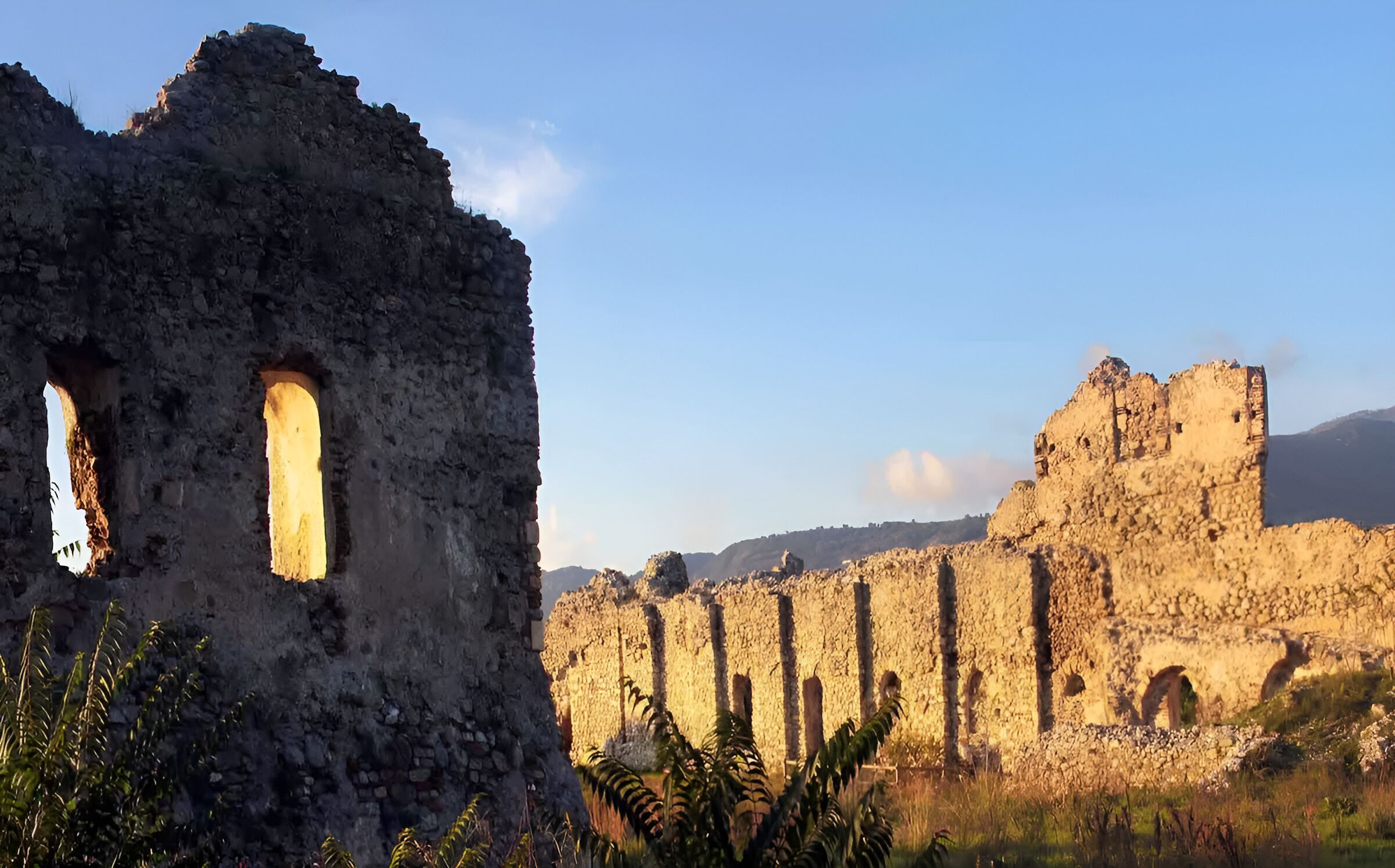Des ruines antiques aux murs de pierre et aux ouvertures en arc de cercle, se dressant sur un ciel dégagé.